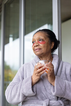 Senior African American woman standing by sliding glass panels in robe with red patches