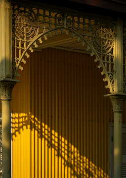 Shadow of a tree branch falls across the yellow wall beneath an arched ironwork trellis of the Palacio de Ferro, Luanda Province, Luanda, Angola