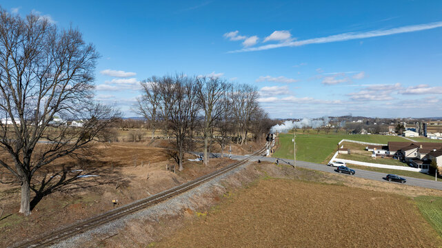 Train Travels Through Rural Area With Trees and Fields in View During Daytime With Clouds Overhead