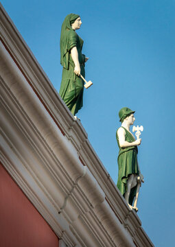 Two allegorical statues holding a hammer and a caduceus stand on the roof cornice of a historic building, Luanda Province, Luanda, Angola
