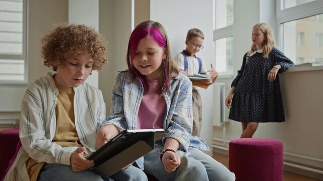 Caucasian children playing educational game on digital tablet and celebrating in school hallway. Clip portrays edtech advertising, mobile school app promo, and digital learning campaigns
