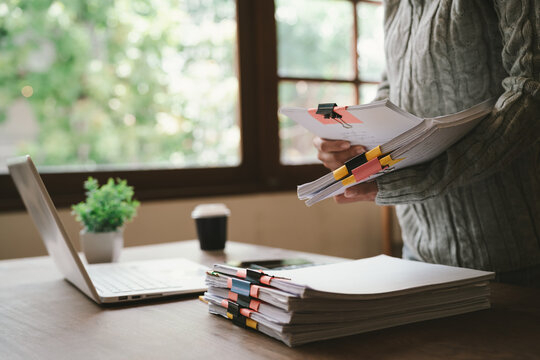 A close-up shot of an Asian woman handling a large volume of documents and files, dealing with organization, management, deadlines, workload, bureaucracy, and business responsibilities.
