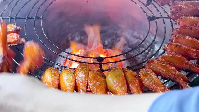 Delicious grilled chicken wings on skewers over a hot charcoal grill at a night market stall. Authentic Asian street food freshly cooked over open flames. Tasty barbecue appetizer.