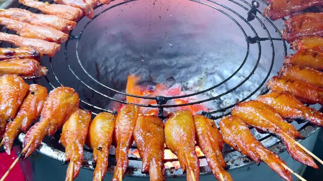 Delicious grilled chicken wings on skewers over a hot charcoal grill at a night market stall. Authentic Asian street food freshly cooked over open flames. Tasty barbecue appetizer.