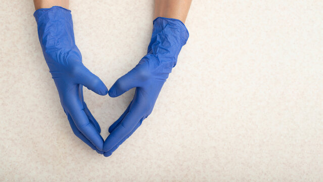 Caucasian hands in medical gloves showing heart shape gesture over flat table with copy space
