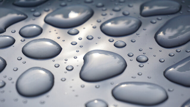 Water droplets on smooth gray surface forming abstract pattern, highlighting purity, freshness, surface tension and clean minimal background for hygiene, technology or design concepts.