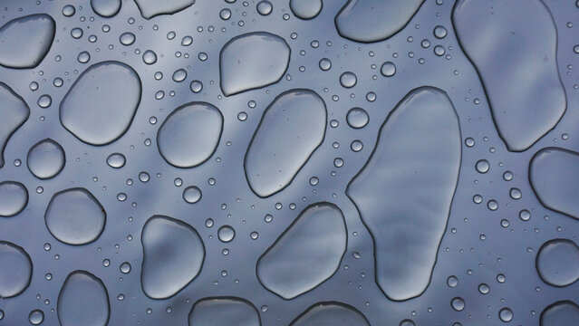 Water droplets on smooth gray surface forming abstract pattern, highlighting purity, freshness, surface tension and clean minimal background for hygiene, technology or design concepts.
