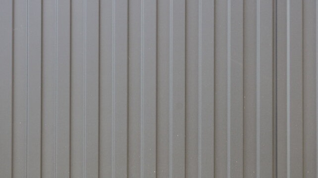 Surface made of brown profiled metal sheeting; uniform texture of corrugated wall paneling with vertical ribs. Used for cladding facades, fences, and rapidly assembled structures