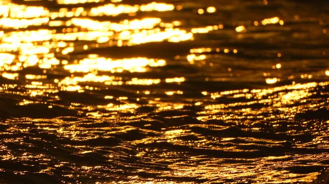 Radiant golden sunlight gleaming intensely across dark rippling ocean waves during sunset. Macro close-up shot.