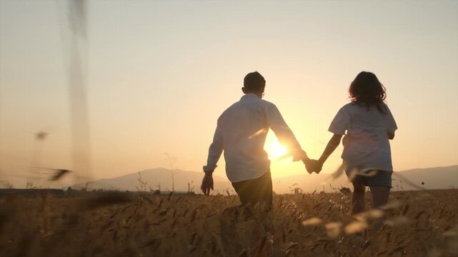 A happy young couple runs hand in hand toward the sunset through a wheat field in the mountains, experiencing joy and appreciating simple moments together. Happiness, simple moments, appreciating life