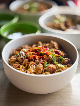 Vertical macro shot of Indonesian chicken noodles mie ayam in a white bowl with a blurred background