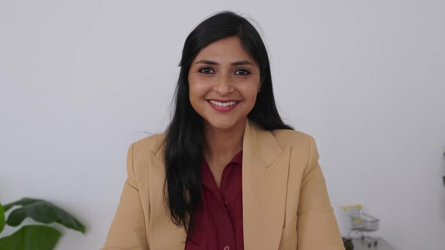 Portrait of happy mid adult Indian businesswoman smiling at camera in office. Professional portrait showing confidence and positive attitude. Success and empowerment concept.