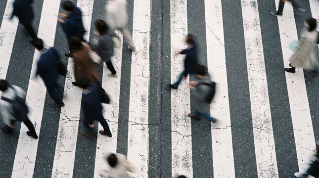 Dynamic high-angle view of a diverse group of urban professionals and commuters briskly crossing a busy city zebra crossing, capturing the energetic pulse of modern life