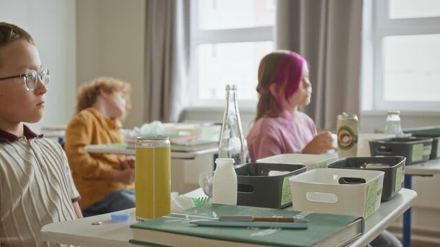 Caucasian school children sitting at desks during environmental education class with waste sorting containers. Footage suits green education campaigns and sustainability advertising