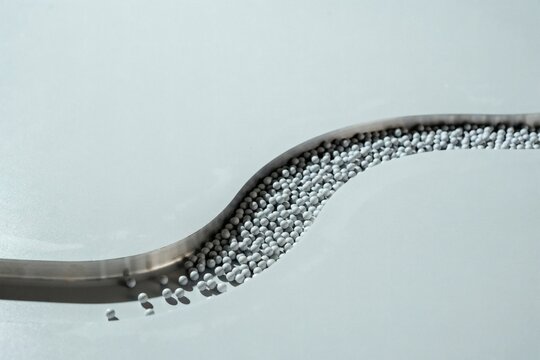 White pellets gathered along a brushed steel s-curve on a pale grey surface