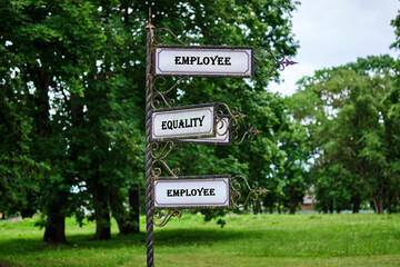 A signpost displays the words employee and equality in a park. The setting features trees and grassy areas © Garik