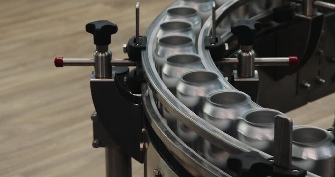 Empty metal beer cans travel around curved conveyor in packaging facility. Automated guides maintain spacing directing containers toward next processing stage