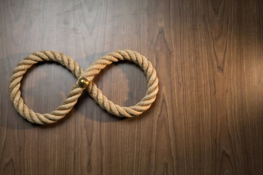 Jute rope tied in a figure eight loop with a brass pin on dark walnut