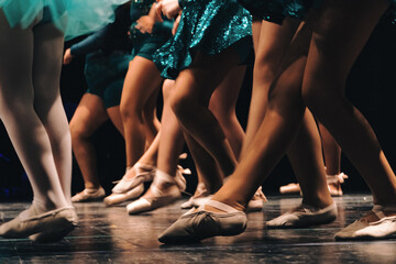 Dancers' legs and feet in ballet slippers performing a routine on a dark stage, showing movement and grace © Manuel