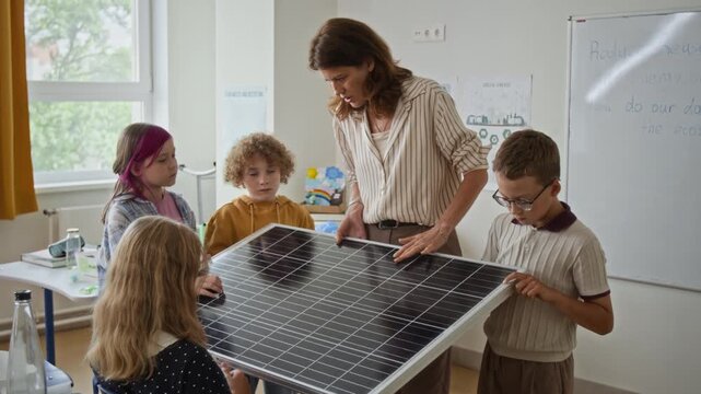 Caucasian female teacher demonstrating solar panel to school children during science lesson in classroom. Ideal for green energy education, STEM learning, and sustainability marketing