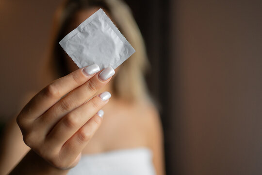 Safe prophylactic AIDS prevention, contraception concept. Female hand holds condom in package, selective focus. Having safe love for male and female.