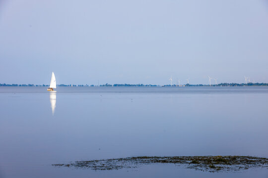 A tranquil scene of a sailboat gliding on peaceful waters at Rondeau Provincial Park in Ontario with wind turbines lining the distant horizon.