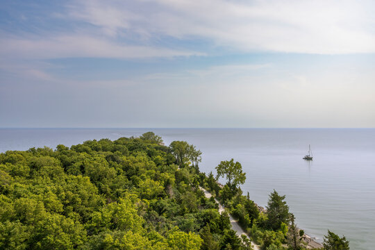 A breathtaking view from Point Pelee's lookout tower, capturing lush forests, serene waters, and a solitary sailboat in Ontario's beautiful national park.