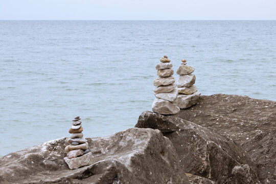 Stone inukshuks on Pelee Island, Ontario, stand on rugged rocks beside the calm lake.