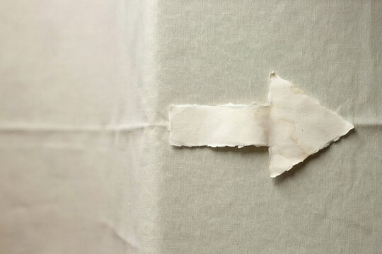 Torn handmade paper arrow pointing right on a soft linen background