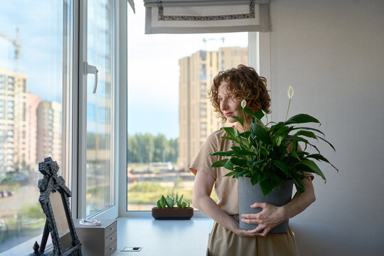 Woman holding a potted peace lily by the windowsill.