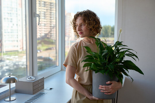 Woman holding a potted peace lily by the windowsill.