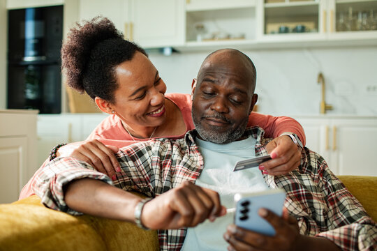 Happy mature couple making mobile payment at home kitchen