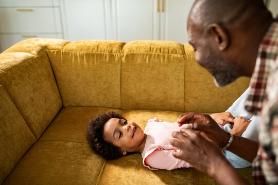 Playful parent tickling child on sofa at home