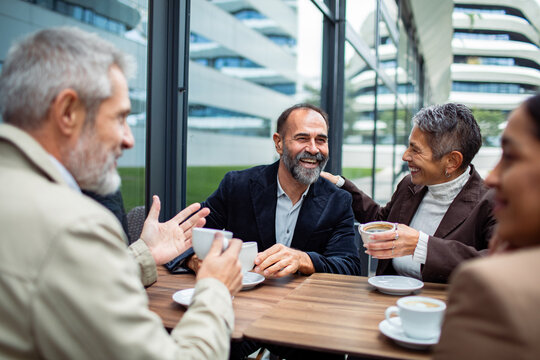 Mature friends laughing over coffee at outdoor city cafe