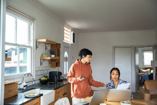 Two women reviewing household bills at home kitchen table with laptops