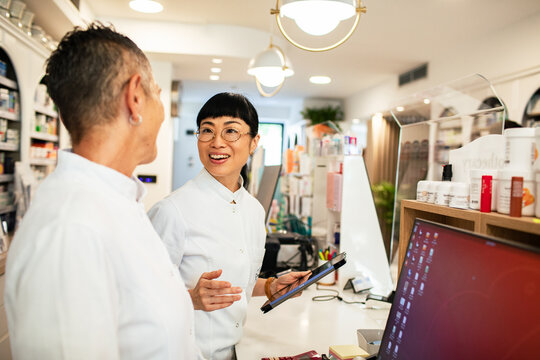 Pharmacists discussing prescriptions with tablet at modern pharmacy counter