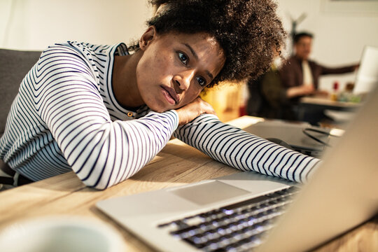 Tired young woman leaning on laptop at office desk