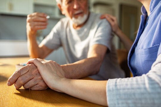 Caregiver holding senior man's hand at home
