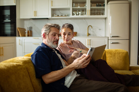Senior couple using smartphone and tablet on sofa at home