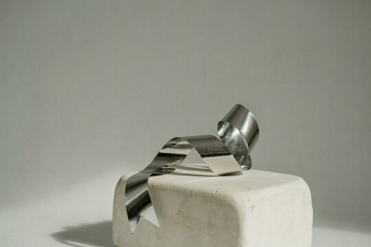 Chrome ribbon draped across a pale stone cube in soft studio light
