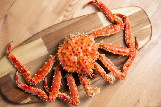 Whole cooked king crab on a wooden cutting board, rustic seafood preparation, gourmet plating, food styling.
