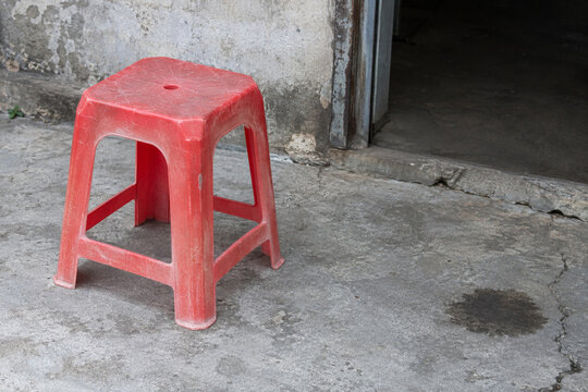Sun Faded Red Plastic Stool outside a Dark Doorway