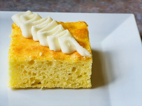 Slice of yellow tres leches cake topped with piped white frosting served on a ceramic plate