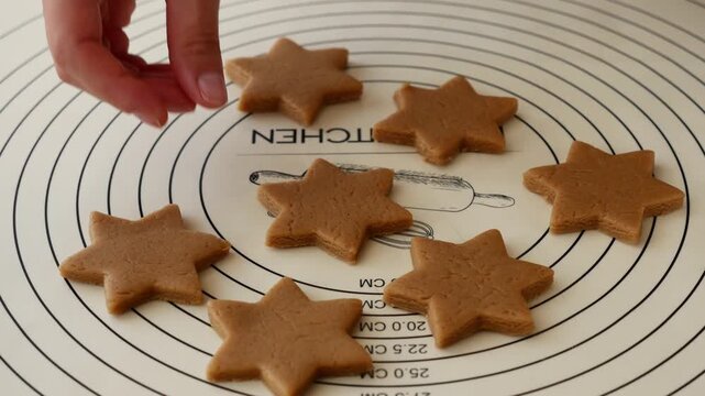 Close-up of woman picking up star shaped gingerbread cookie during Christmas Baking at home.