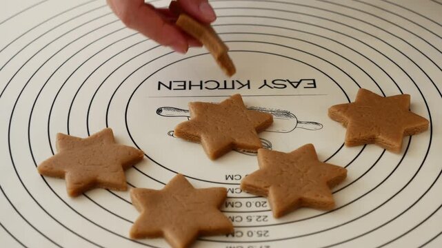 Woman picking up star shaped gingerbread cookie dough during Christmas baking.