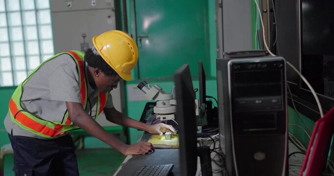 Quality inspector examining small metal component under stereo microscope in factory lab