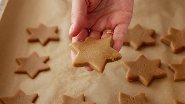 Close-up of woman placing homemade gingerbread star cookies on parchment paper for baking.