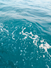 Fototapeta premium Texture of clear blue sea water ripples with white foam from boat waves