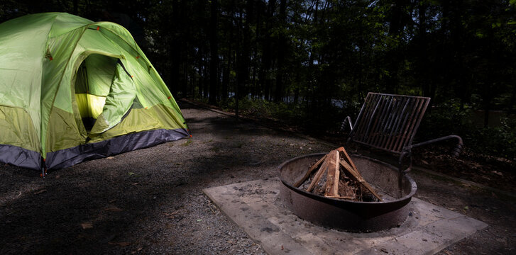 Dome tent in the woods at dark with wood ready to burn for a campfire