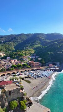 Coastal village with pebble beach and rows of umbrellas by turquoise water.  Monterosso al Mare, Italy